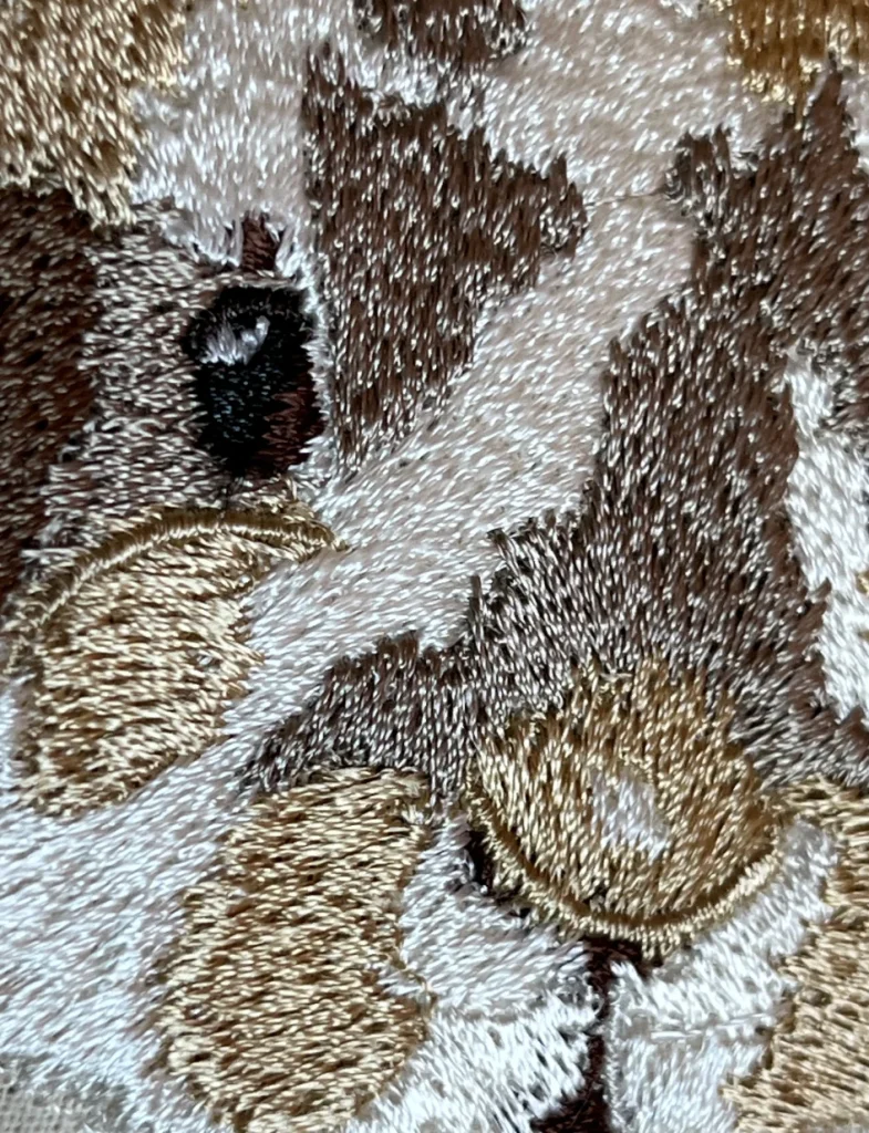 Gros plan détaillé sur les points de broderie d'un tote bag personnalisé, montrant la texture des fils beige, blanc et marron formant un pelage de lapin